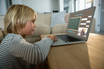 Smiling caucasian boy using laptop for video call, with class on screen