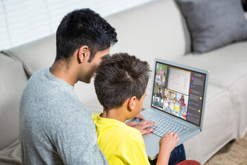 Biracial boy with father using laptop for video call, with elementary school pupils on screen