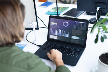 Caucasian businesswoman sitting at desk using laptop with graph and statistical data on screen