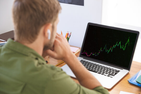 Caucasian businessman sitting at desk using laptop with graph and statistical data on screen