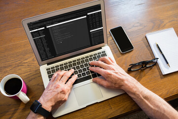 Hands of caucasian male programmer siting at desk, using laptop with coding on screen