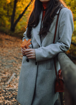 Close up of womans coat at the street without face. Girl with maple leaf in fall