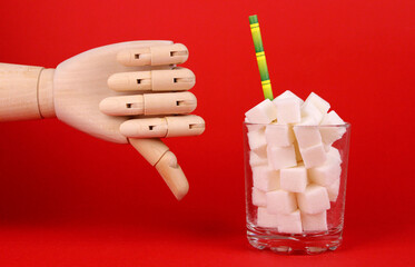 Limited sugar intake. Sugar diet. Sugar cubes in glass and wooden hand with negative gesture on red...