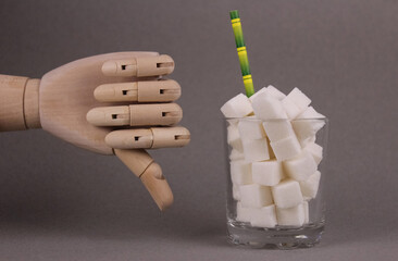 Limited sugar intake. Sugar cubes in glass and wooden hand with negative gesture on gray background
