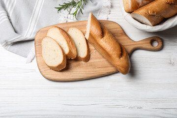 Cut tasty baguette with rosemary on white wooden table, flat lay