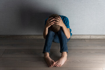 Above view of boy sitting on the floor in dark room and protects head with his hands. Abusing, home violence concept