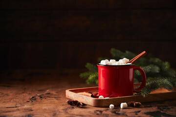 Red cup of hot cocoa with marshmallows on wooden table with christmas tree for christmas