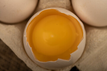 White chicken eggs and one broken egg in a tray made of white cardboard, close-up selective focus.