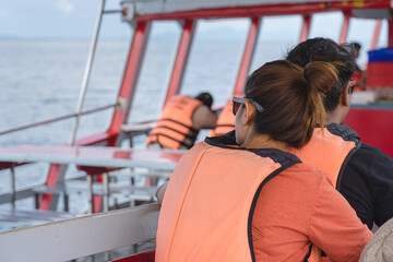 Back view of lover passengers in life vest relaxing on balcony enjoying view from boat of Samui island in sea.Happy casual couple tourists outside on tropical holiday destination.Cruise ship vacation.