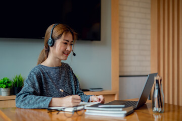 Young attractive university student using a laptop computer, studying online at home. Cheerful caucasian asian woman writes notes, planning working process, sitting at home. Exam preparation. 