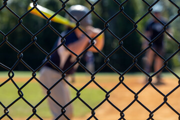 Little league batter out of focus in the background while the backstop is in focus - obrazy, fototapety, plakaty