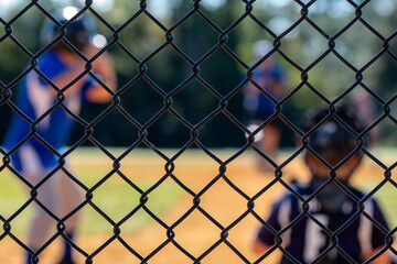Little league batter out of focus in the background while the backstop is in focus - obrazy, fototapety, plakaty