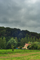 House with an off road vehicle on the edge of a hilly forest under a dark cloudy sky.