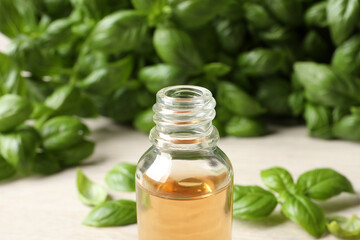 Glass bottle of basil essential oil and leaves on white table, closeup