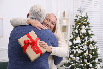 Obraz na płótnie Canvas Happy mature couple with gift box hugging at home. Christmas celebration