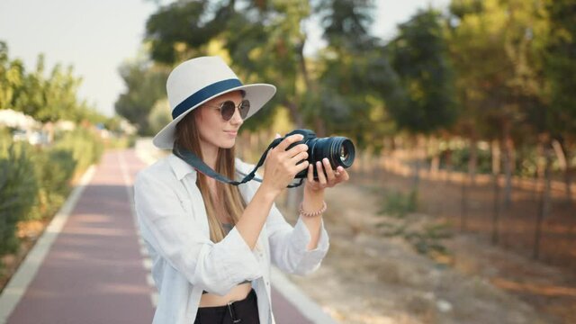 Fashion look, pretty cool young woman model with camera wearing a elegant hat, outdoors over. Photo of happy excited emotional young woman photographer tourist standing holding camera.