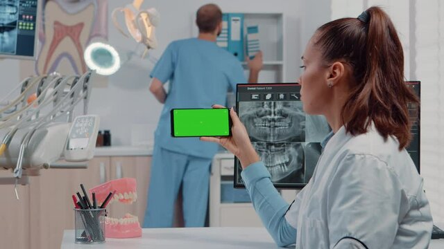 Woman working with horizontal green screen on mobile phone for teethcare in dentist office. Orthodontist looking at chroma key and mockup template on smartphone for dental care.