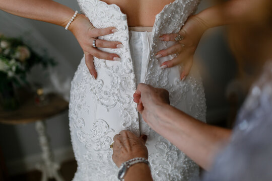 Mother of the bride zipping up a wedding dress before the ceremony  close-up Bride getting ready detail of woman's hand helping to close zipper on white wedding dress Bride putting on her dress 