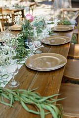 Detail of a table set for wedding banquet white rug runner on a wooden table Green floral decoration brown plates Close up Beautiful table setting for wedding celebration Green branch and fresh flower