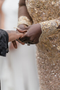 The African American Bride In Goldish Wedding Dress Puts A Wedding Ring On Her African American Grooms Finger Wedding Ring With Diamond Long Nails