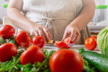 Chef slicing tomato using knife on the table in restaurant. Process of cutting and preparation food in kitchen.