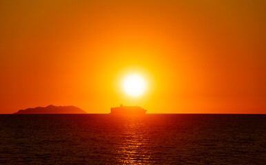 A backlit passenger ship near an island at sunset