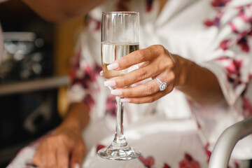 Bride in flourish robe holding a glass of champagne Morning of the bride Joyful bride close-up cropped view Diamond ring on her finger Blurred background