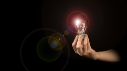 Hand of woman holding illuminated light bulb in black background. Idea, innovation, thinking and inspiration for business concept photo