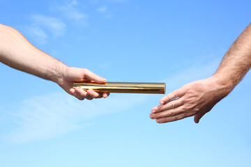 Man passing baton to his partner against blue sky, closeup