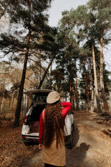 girl with long hair stands in the autumn forest against the background of a large car