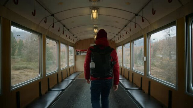 Male traveller, hipster travel blogger or content creator, tourist with backpack pass through moving train carriage in picturesque mountain scenery. Cinematic adventure destination