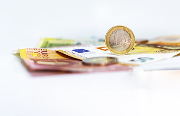 A used 1 euro coin standing on top of some euro banknotes