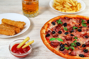 Pizza on a platter close-up on a white wooden table with ketchup, juice, sauce and potatoes.