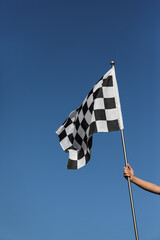 Woman holding checkered finish flag on light blue background, closeup