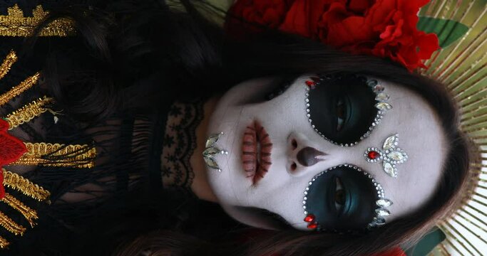 Vertical portrait of young woman with sugar skull makeup and red roses dressed in black costume of death as Santa Muerte. Day of the Dead or Halloween concept.