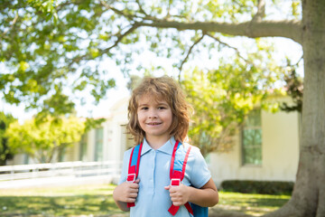 Schoolboy with backpack walks on green lawn. Elementary school and education. Kids from primary school. Portrait of Pupil near school.