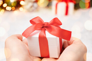 Christmas gift box with red bow in woman hands on the background of Christmas tree and snow