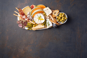 Assorted cheeses on wooden board plate, olive, grapes, bread on black stone background, top view,...