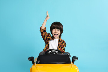 Little child driving yellow toy car on light blue background