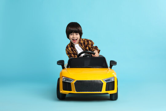 Little child driving yellow toy car on light blue background