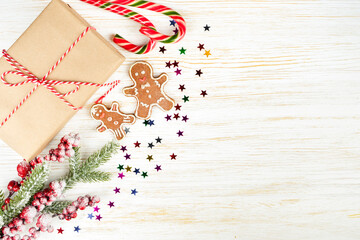 New year background with christmas tree branch, gingerbread man and gift box on white wooden background with copy space. Festive mockup, flat lay, top view.