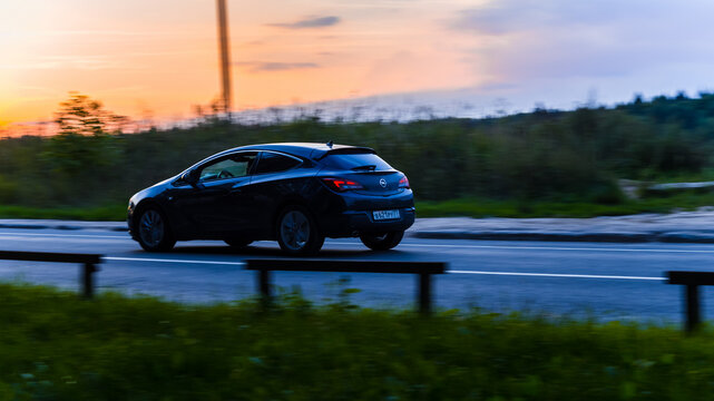 Opel Astra J GTC driving on the country road at dusk. Side view of black hatchback in motion on the sunset sky background