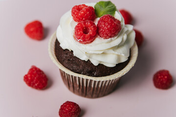 Cupcake with white butter cream and berries lies on a pink background. Cakes with raspberries and cream.