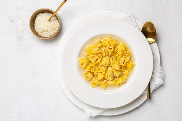 Tortellini. Pasta stuffed with a mix of meat, and parmigiano cheese and served in capon broth. Top view, white background. - obrazy, fototapety, plakaty