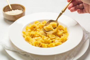 Eating tortellini. Pasta stuffed with a mix of meat, parmigiano cheese and served in capon broth. Close-up. © Olga