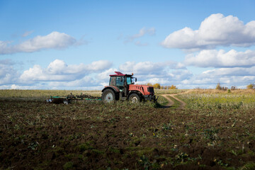 Obraz premium A farmer in a tractor, agricultural machinery, prepares the land with a cultivator. A modern red tractor in a field. Plowing a heavy tractor while cultivating agricultural work in a field with a plow.