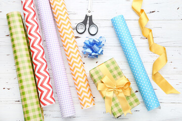 Rolls of craft papers with gift box and scissors on white wooden background