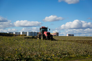Fototapeta premium A farmer in a tractor, agricultural machinery, prepares the land with a cultivator. A modern red tractor in a field. Plowing a heavy tractor while cultivating agricultural work in a field with a plow.