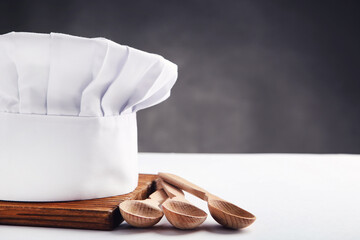 Chef hat with wooden spoons and cutting board on black background