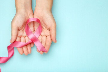 Breast cancer concept. Female hands with pink ribbon on blue background